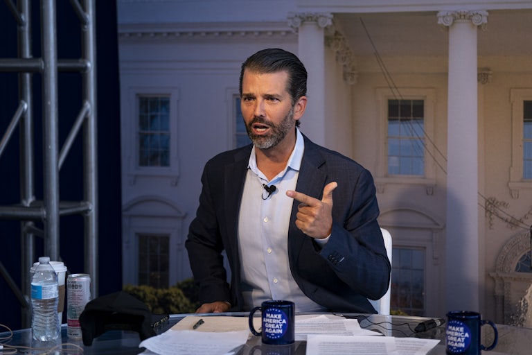 Donald Trump Jr. sits at a table and points his finger angrily