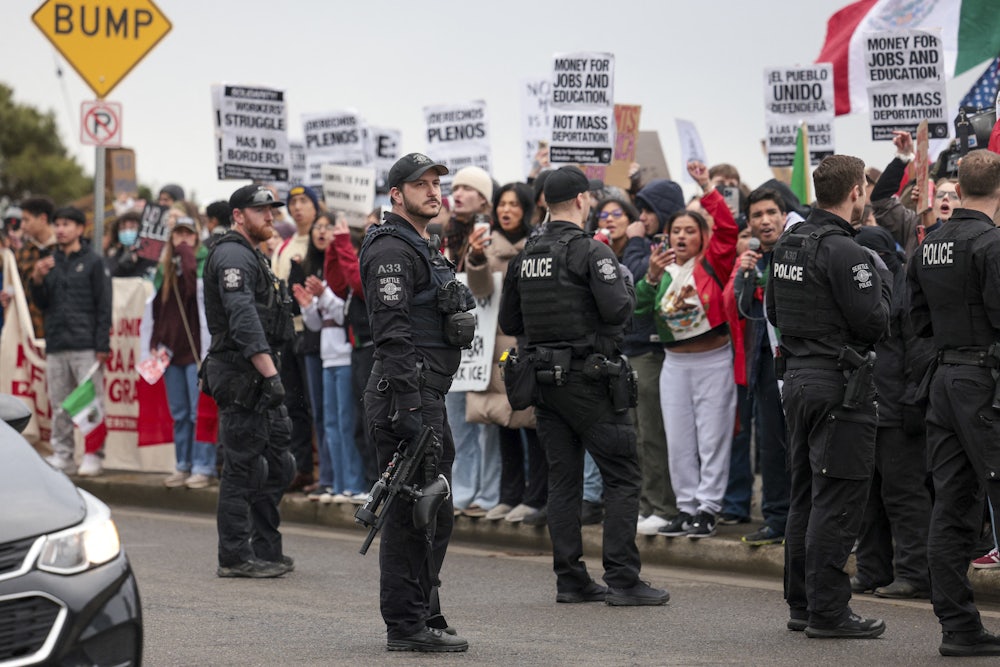 Police stand in the street in front of a line of demonstrators holding anti-ICE signs.