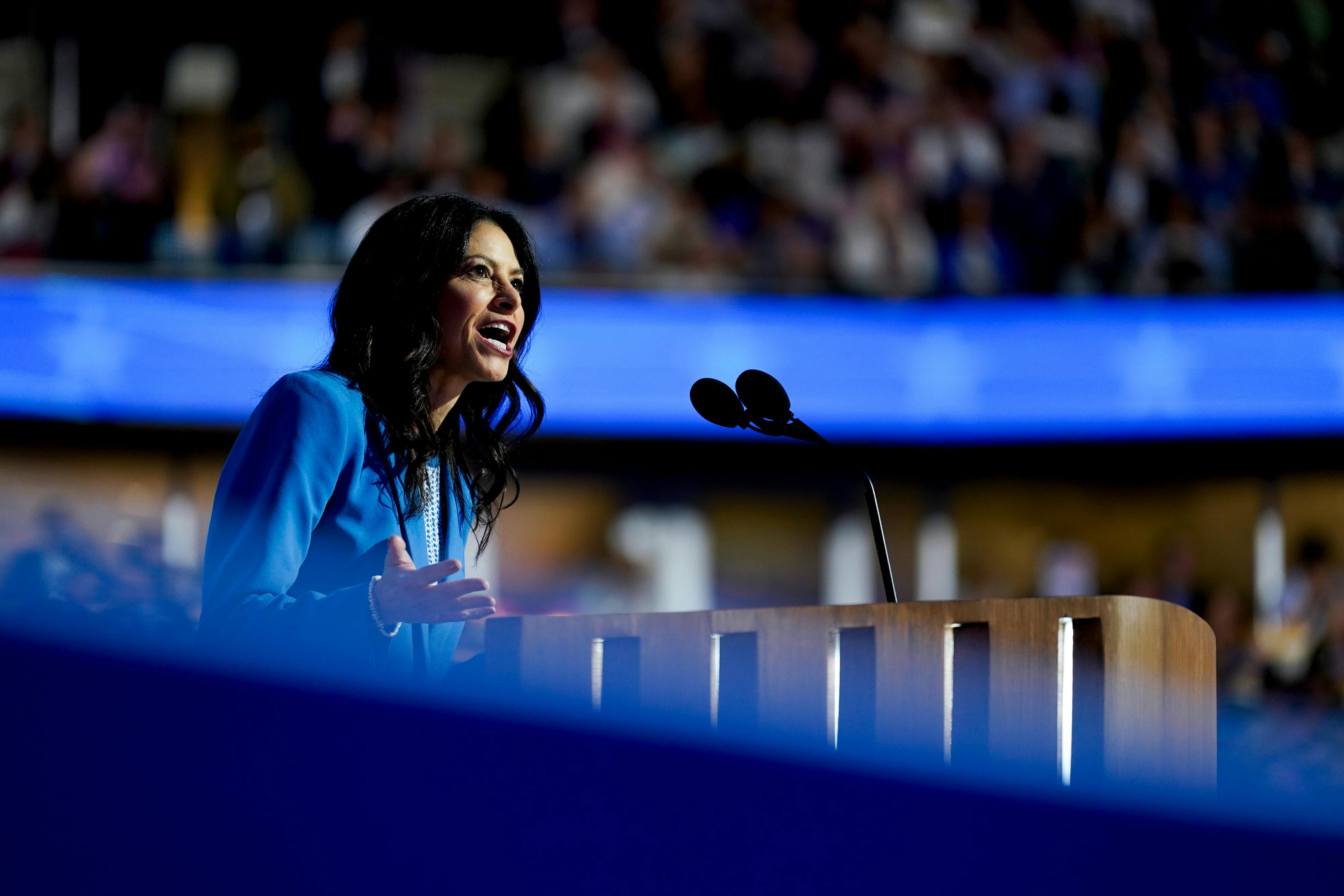 Dana Nessel is seen in profile speaking into a microphone while wearing a blue suit.