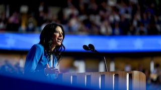 Dana Nessel is seen in profile speaking into a microphone while wearing a blue suit.