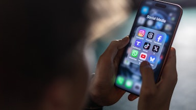 A person holds a smartphone with social media apps on the screen.