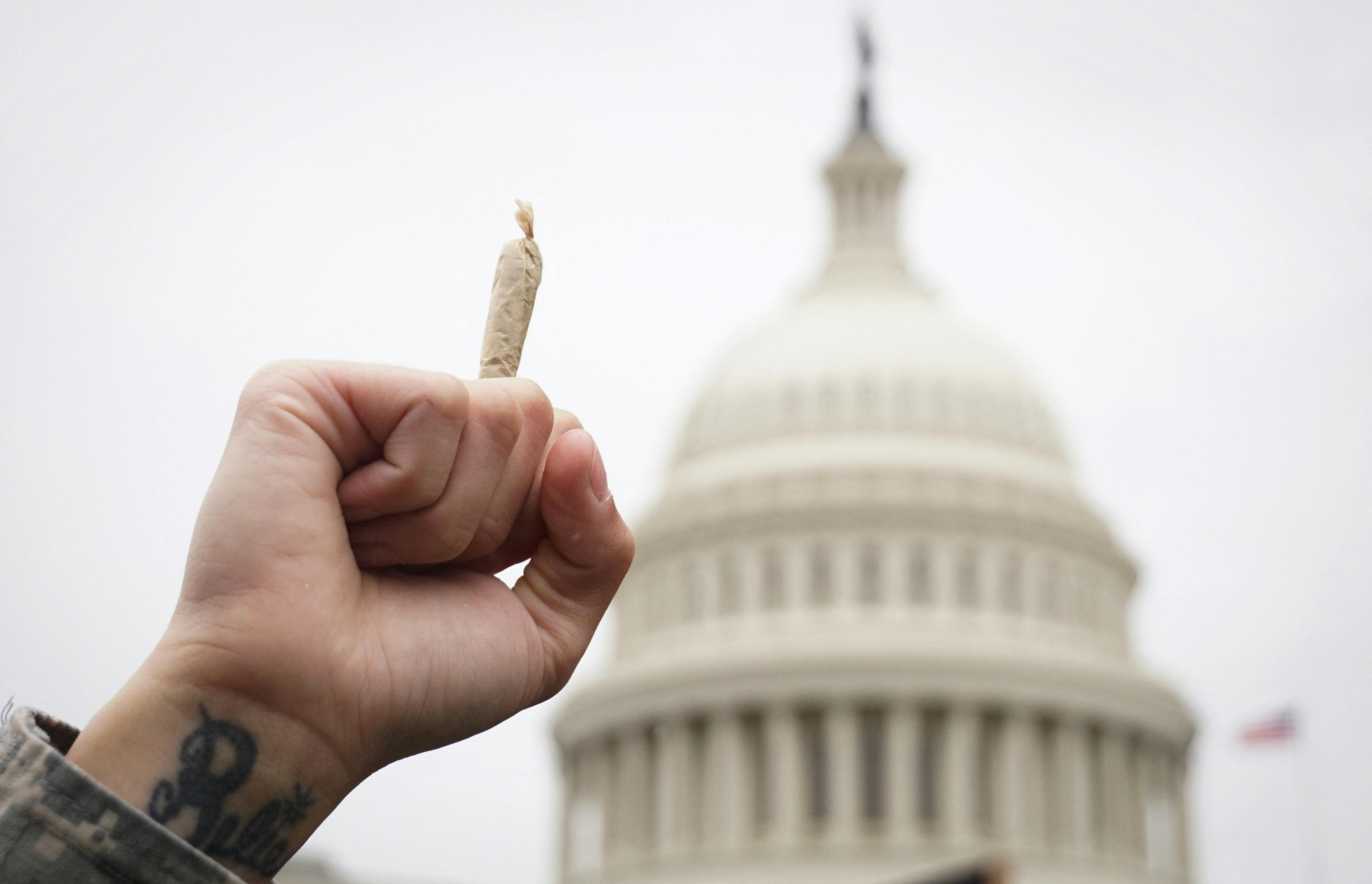 A man holds a joint in the air in front of the Capitol dome in Washington DC. 