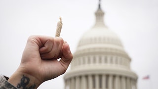 A man holds a joint in the air in front of the Capitol dome in Washington DC.