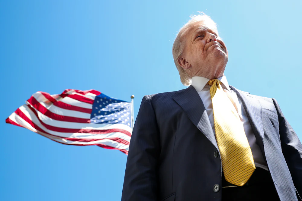 Donald Trump speaks in front of the American flag to the press as he departs the White House.