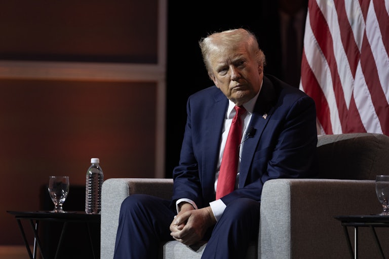 Donald Trump seated on a chair, clasps his hands between his legs
