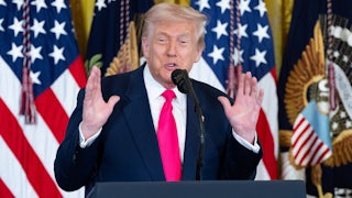 Donald Trump holds up both hands while speaking at a podium