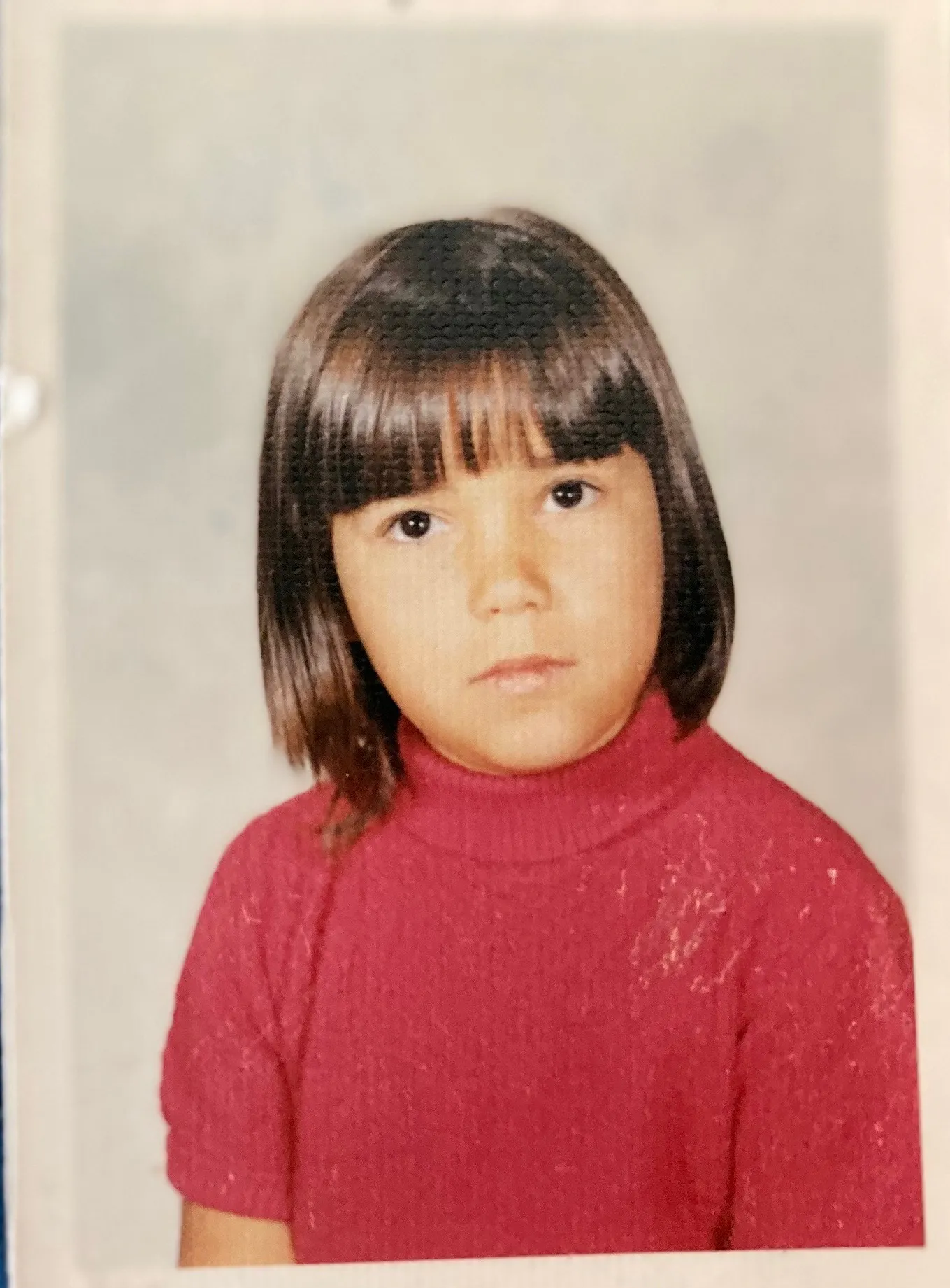 An original studio portrait of the subject, TC, as an eight-year-old girl. She wears a red turtleneck.