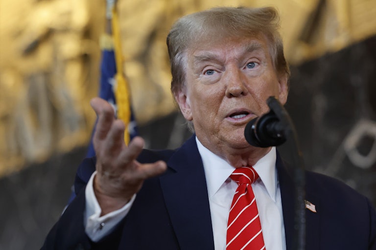 Donanld Trump speaks before a mic, eyebrows raised and arm outstretched toward the camera