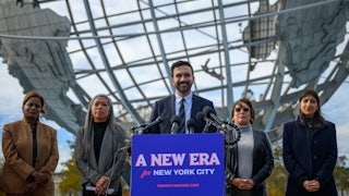 New York City Mayor-elect Zohran Mamdani smiles while standing at a podium with a sign that says "A new era for New York City." He is flanked by his transition team members Melanie Hartzog, Maria Torres-Springer, Grace Bonilla and Lina Khan