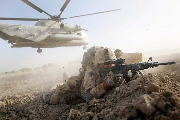An Ameircan marine lines up a rifle while a helicopter flies low behind him