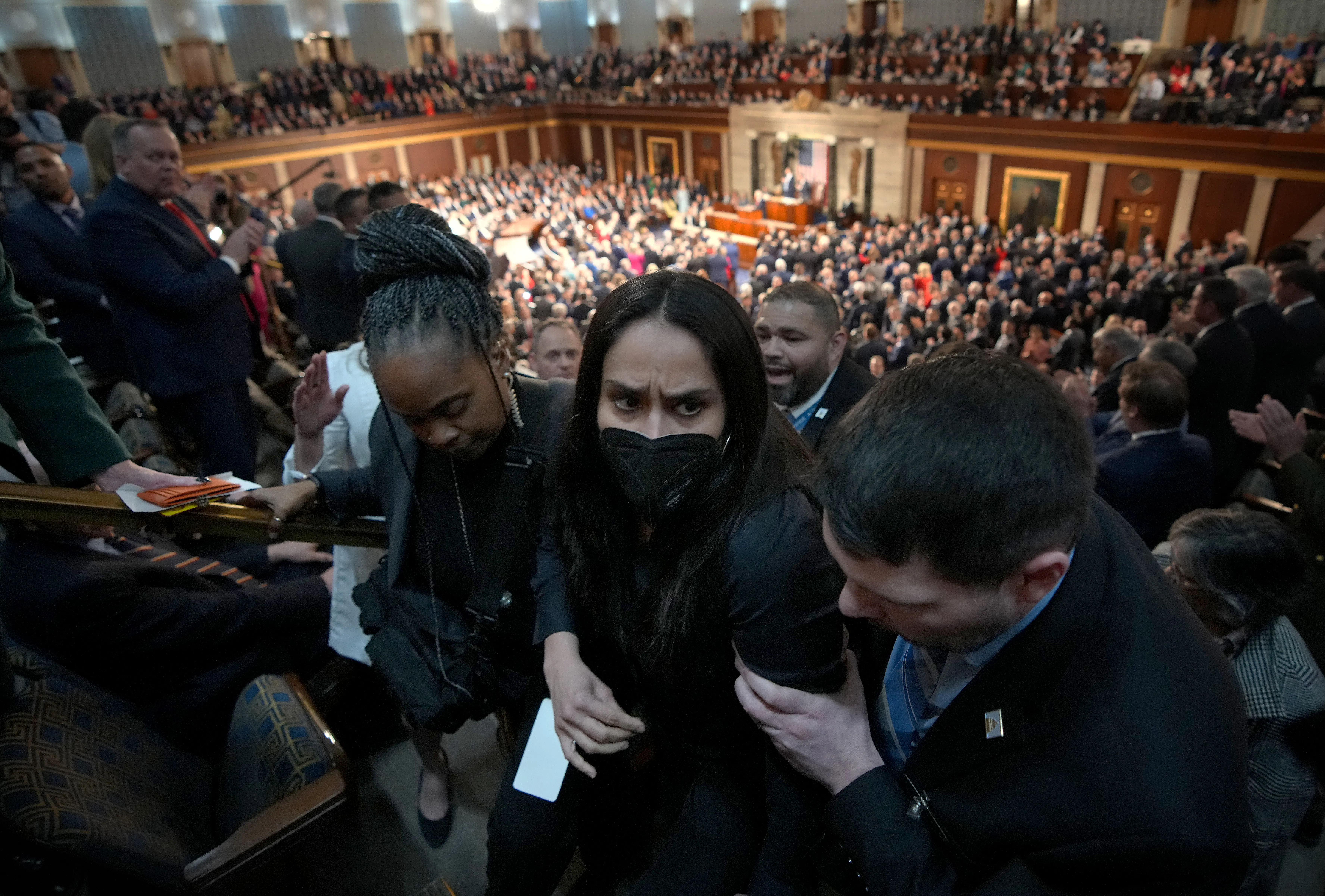 Aliya Rahman, wearing a face mask, is escorted out of the State of the Union by three people.