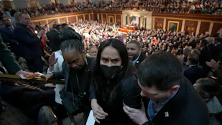 Aliya Rahman, wearing a face mask, is escorted out of the State of the Union by three people.