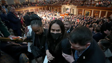 Aliya Rahman, wearing a face mask, is escorted out of the State of the Union by three people.