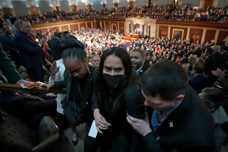 Aliya Rahman, wearing a face mask, is escorted out of the State of the Union by three people.