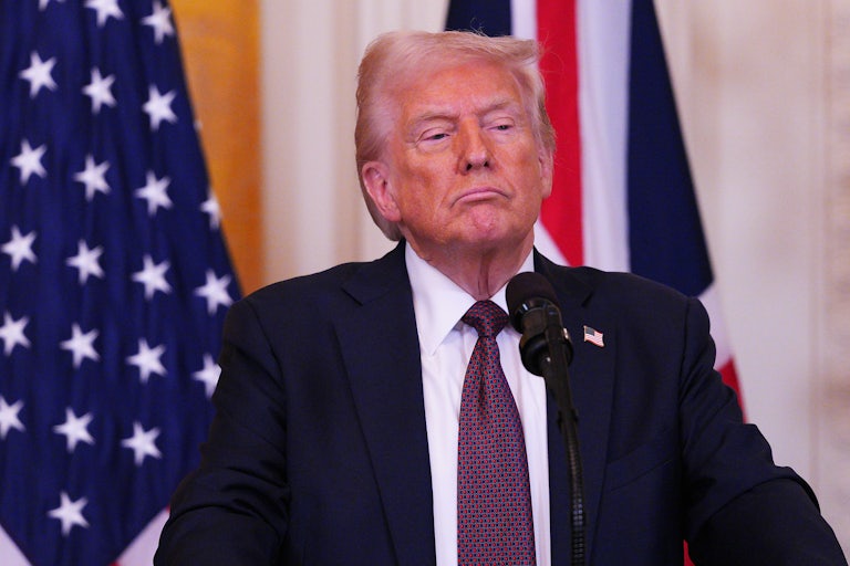 Donald Trump makes a smug face while standing at a presidential podium. A U.S. flag is in the backround.