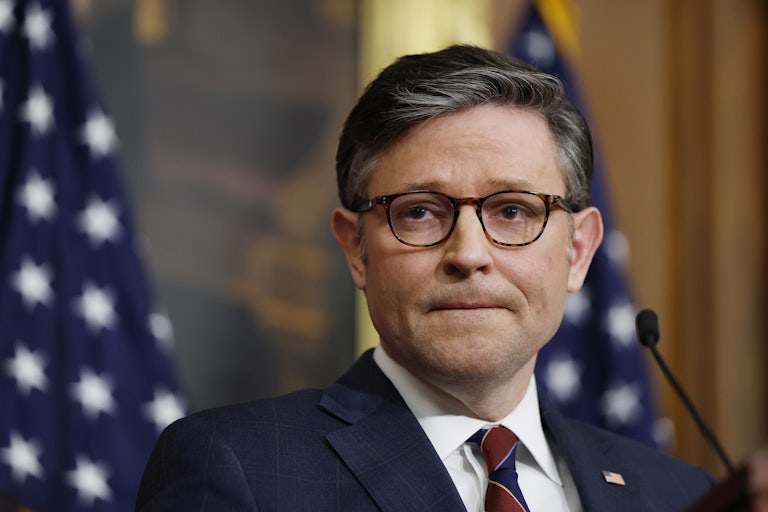 Mike Johnson bites his lip while standing at a podium