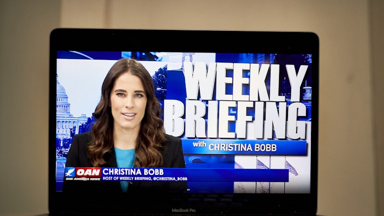 A laptop computer shows Christian Bobb and the words "Weekly Briefing with Christina Bobb" on OANN.