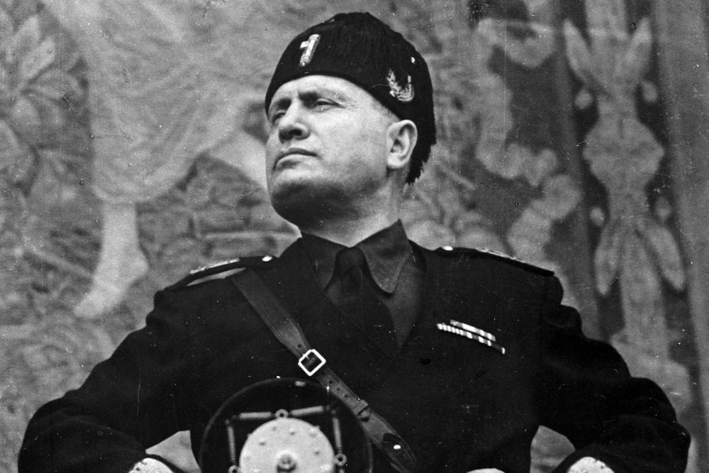 Italian fascist dictator Benito Mussolini stands with his hands on his hips as he stares defiantly into the middle distance.