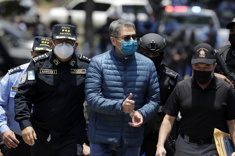 Juan Orlando Hernández, in handcuffs and flanked by police, gives a thumbs up.