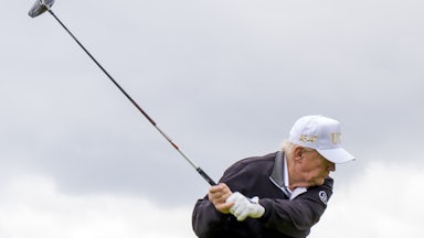 Donald Trump swings a golf club and wears a white USA cap.