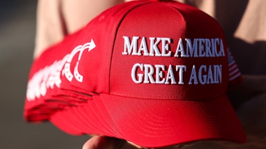 A person holds a stack of Make America Great Again hats.