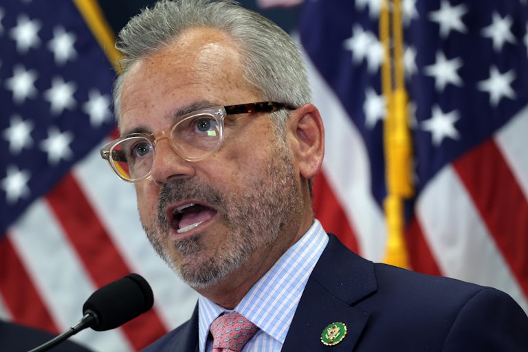 Representative Mark Alford speaks in front of some American flags while wearing clear and black glasses.