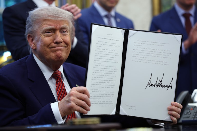 Donald Trump holds up a signed executive order while sitting at his desk in the Oval Office