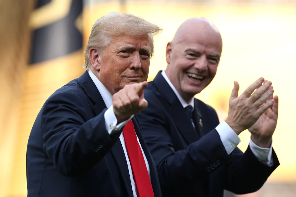 Trump points while Gianni Infantino smiles and claps like a seal behind him