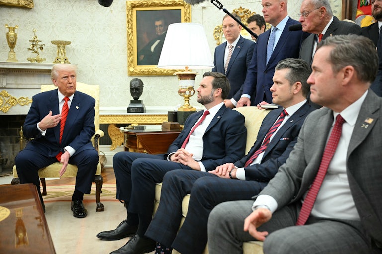 Donald Trump sits in a chair in the Oval Office and speaks, while JD Vance, Pete Hegseth, and Mike Waltz sit on a couch and listen to him