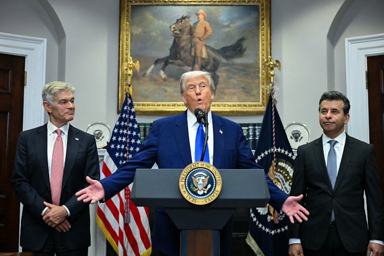 Donald Trump holds his arms out to the side while speaking at a podium in the Oval Office. He is flanked by Mehmet Oz and Marty Makary.