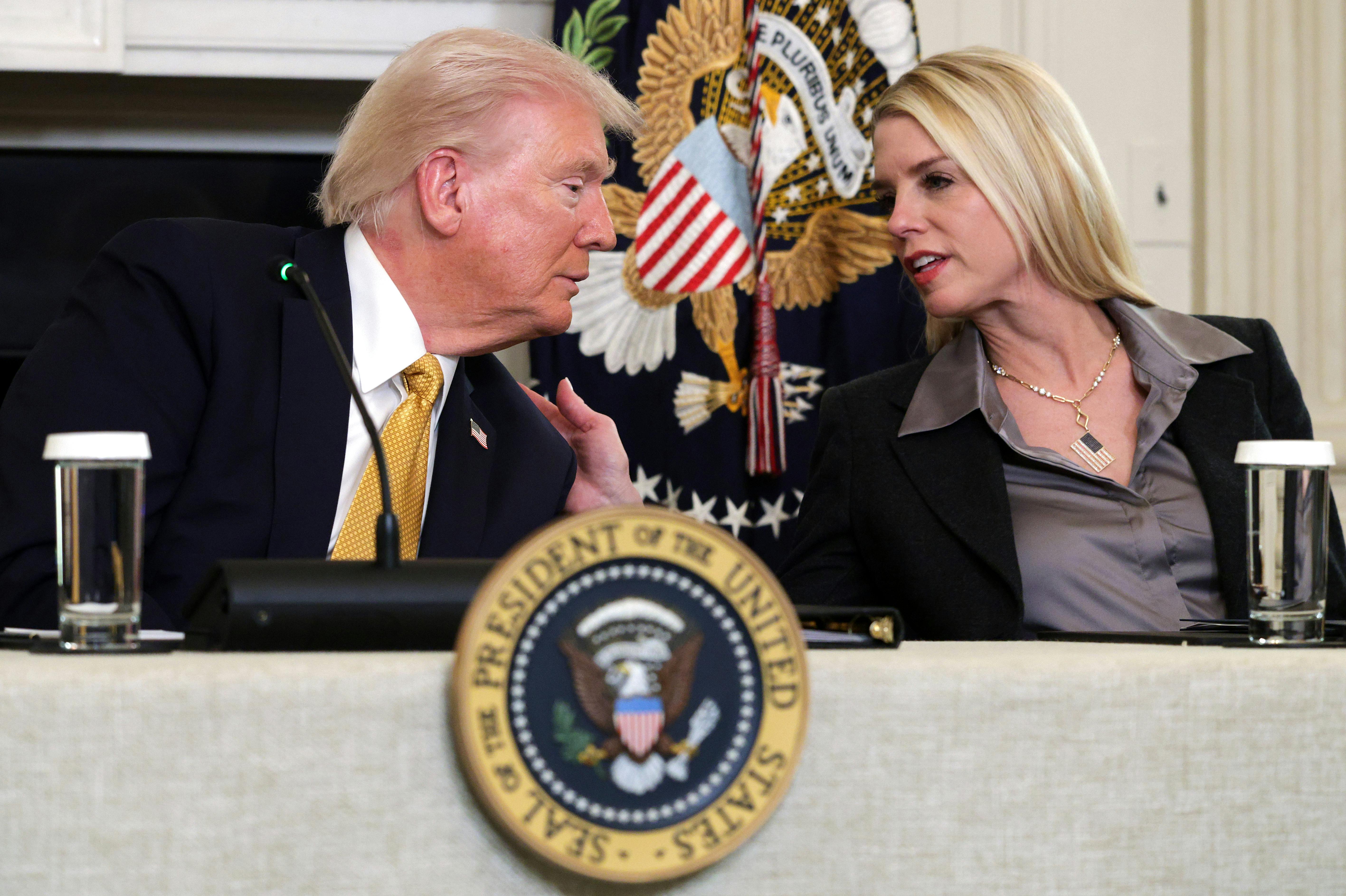 Attorney General Pam Bondi leans over to speak with Donald Trump, placing a hand on his shoulder.