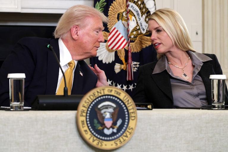 Attorney General Pam Bondi leans over to speak with Donald Trump, placing a hand on his shoulder.