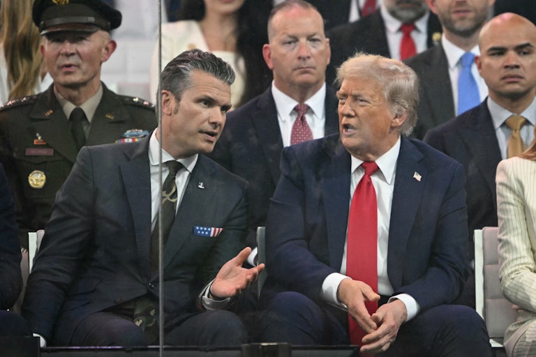 Pete Hegseth and Donald Trump speak while sitting next to each other at the military parade