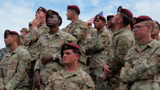A group of U.S. solidiers in fatigues and berets stand while listening to a speech from the president.