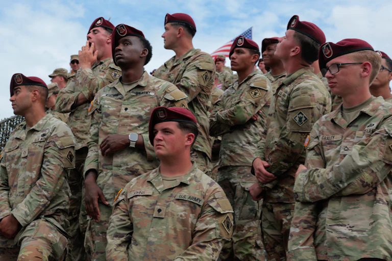 A group of U.S. solidiers in fatigues and berets stand while listening to a speech from the president.