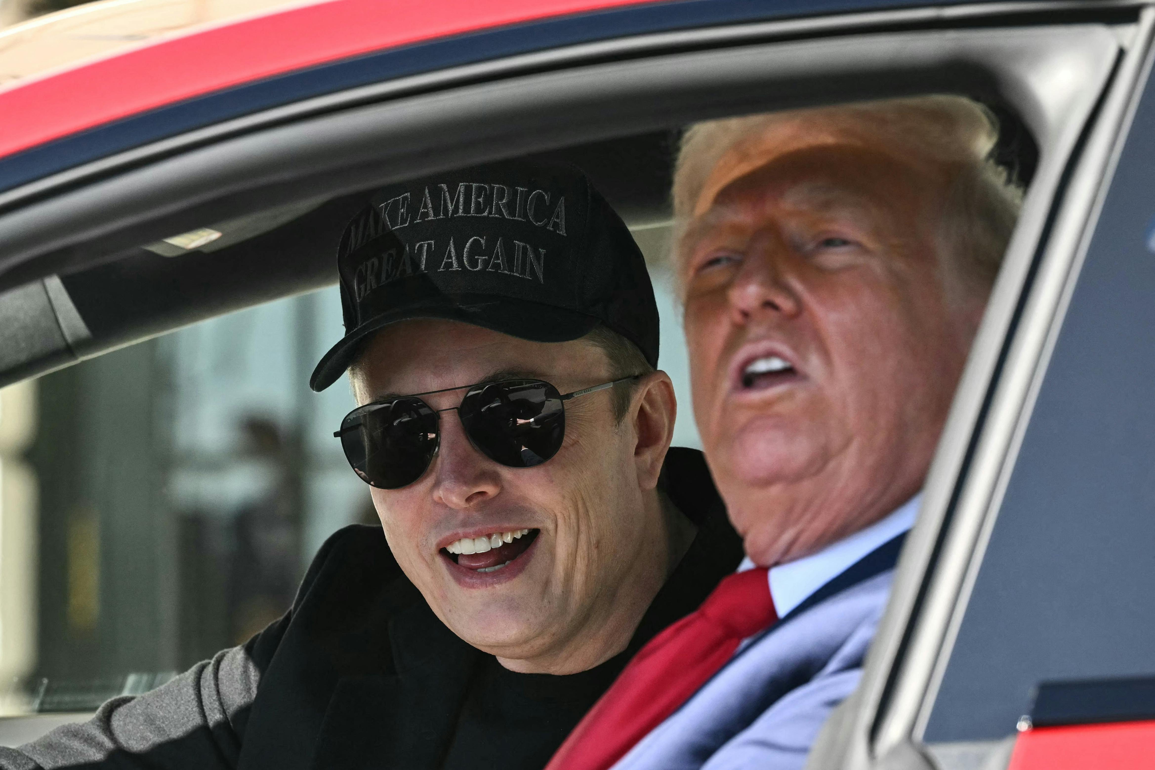 Musk and Trump smile while sitting in a Tesla.