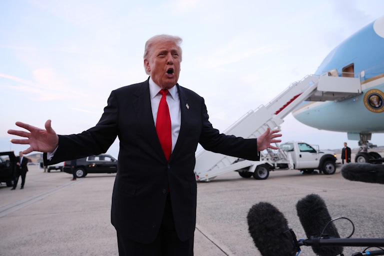 Donald Trump holds his arms out to the side while speaking into microphones on a tarmac