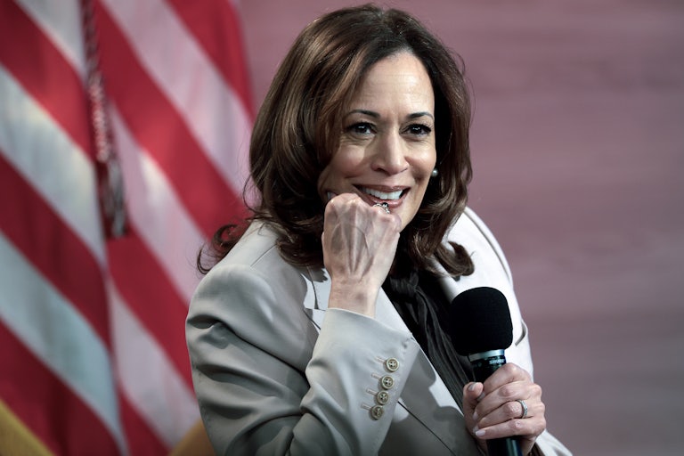 Kamala Harris rests her chin on her fist and holds a microphone
