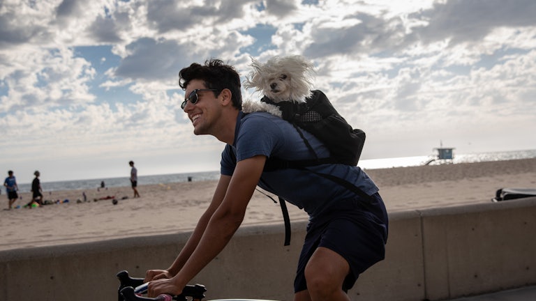 A man bikes with a dog in his backpack along The Strand in Hermosa Beach, CA.