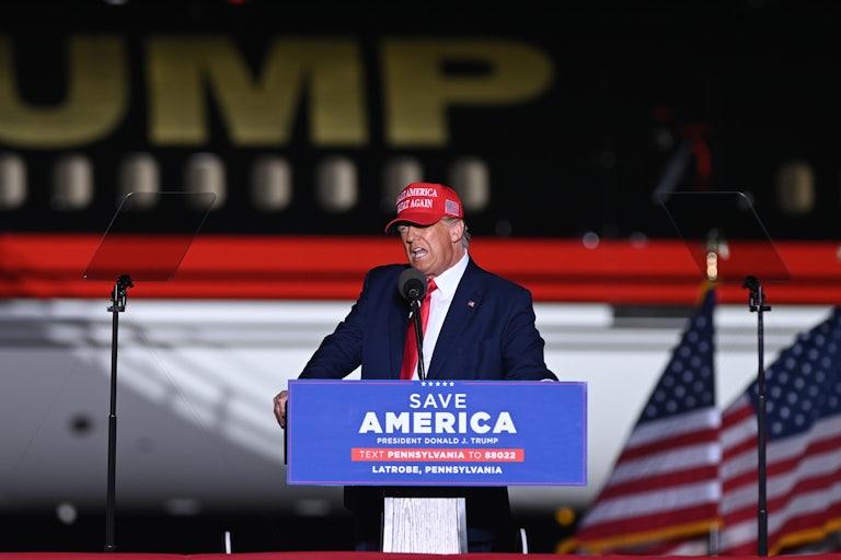 Donald Trump stands at a podium labeled "Save America."