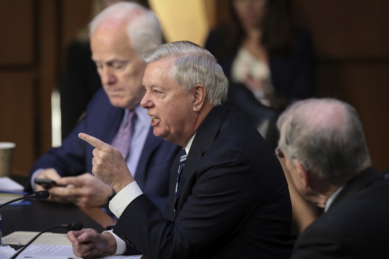 Senator Lindsey Graham speaks in the foreground while pointing a finger. Senator John Cornyn is seated beside him in the background.