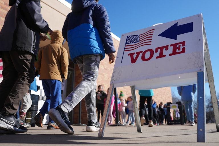 People line up to vote. A sign says "Vote," pointing voters to the polling station.