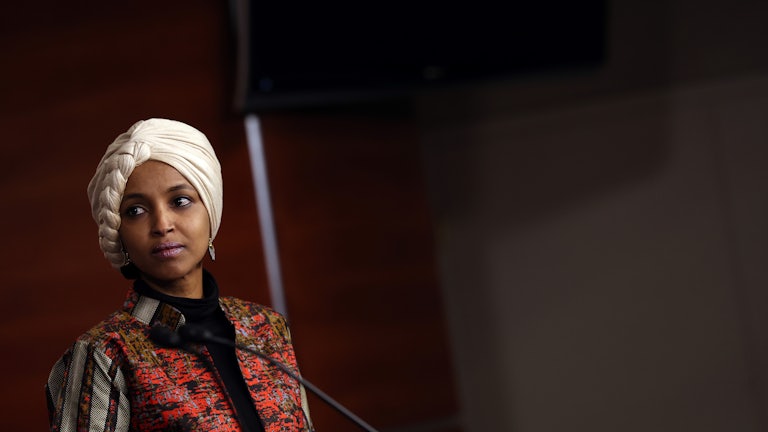 Ilhan Omar stands at a podium and looks to the side