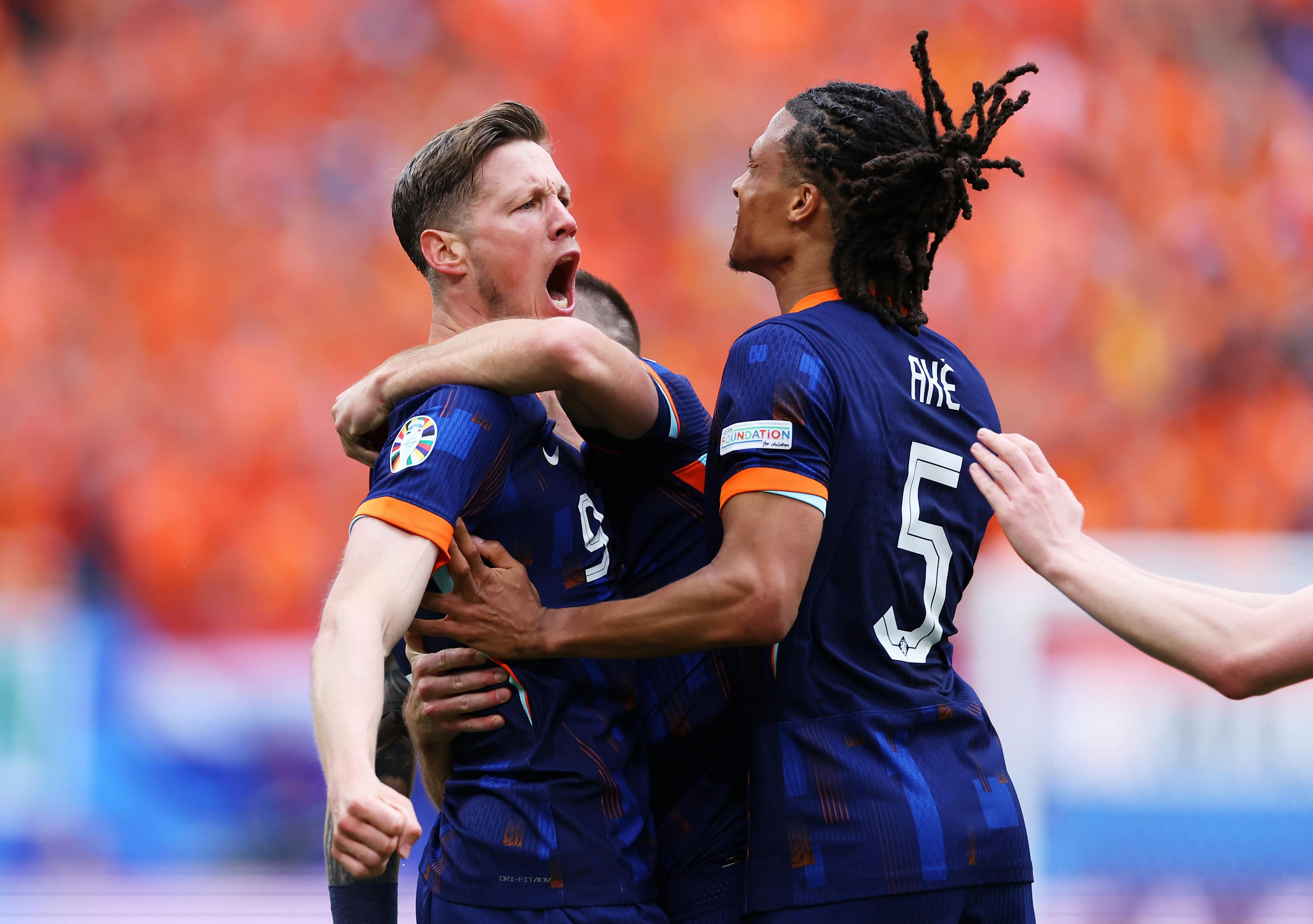 Two soccer players wearing the blue and orange of their country celebrate a goal and hug each other. 