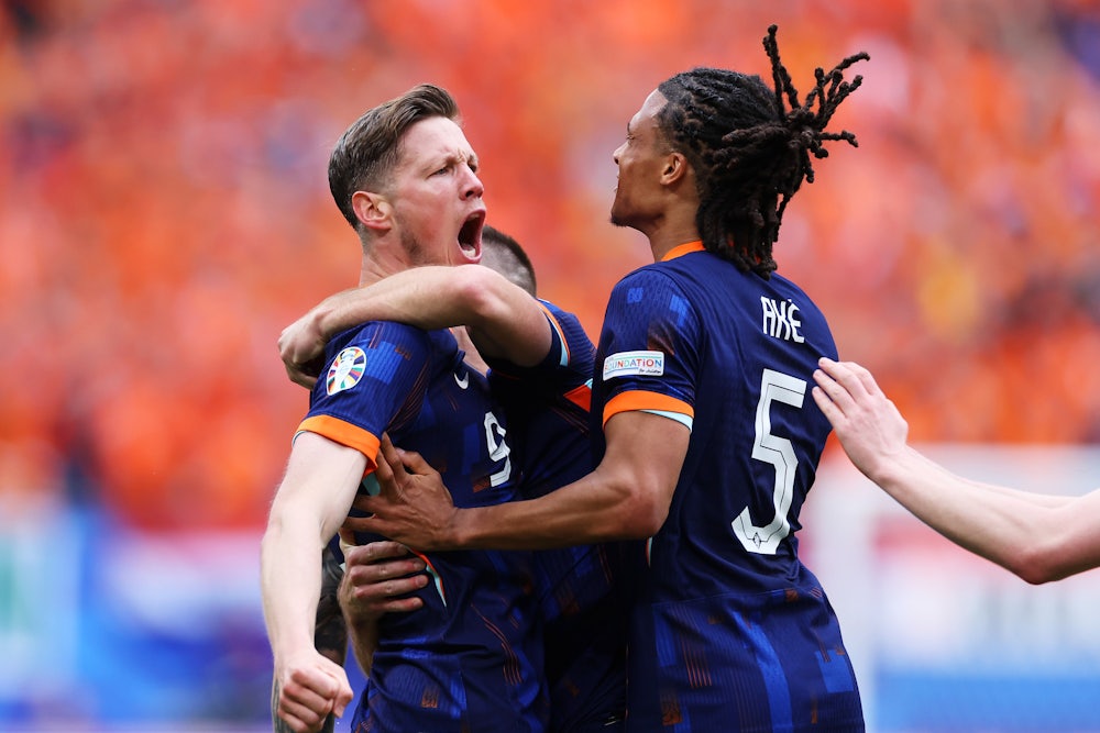 Two soccer players wearing the blue and orange of their country celebrate a goal and hug each other.