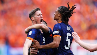 Two soccer players wearing the blue and orange of their country celebrate a goal and hug each other.