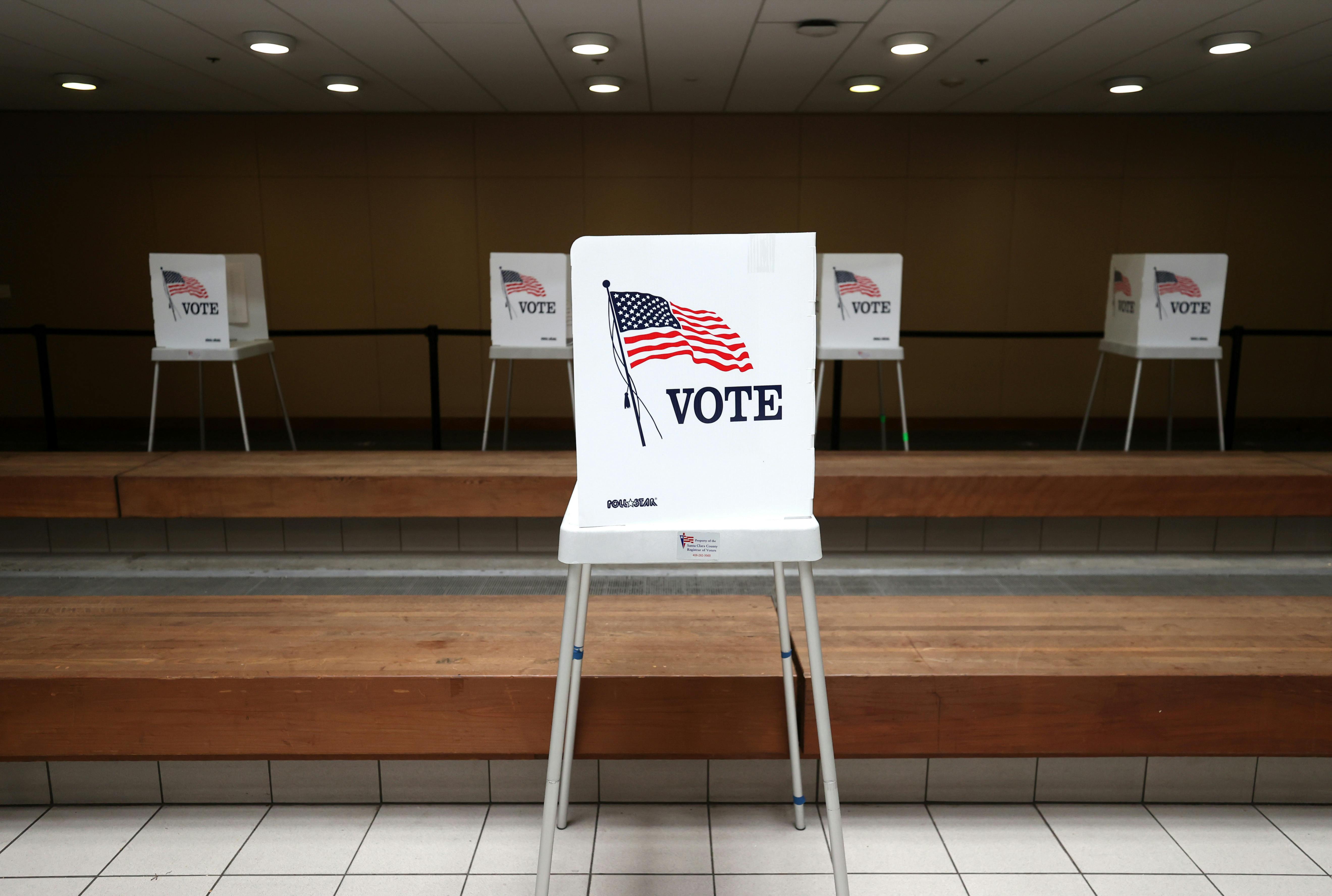 A lone voting booth stands in the foreground at a polling location.