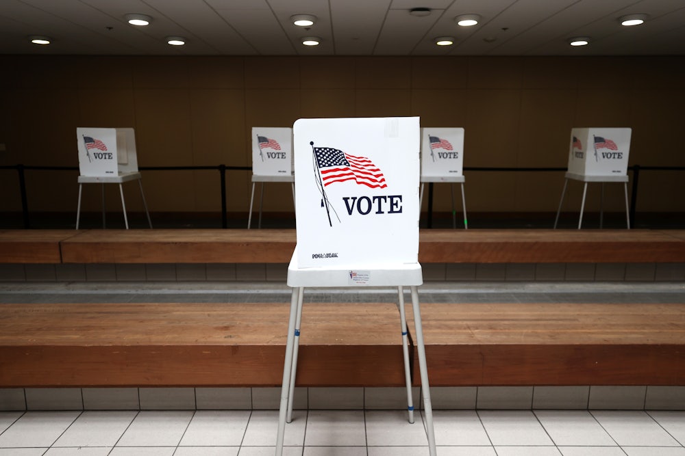 A lone voting booth stands in the foreground at a polling location.