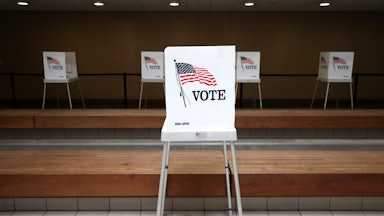 A lone voting booth stands in the foreground at a polling location.