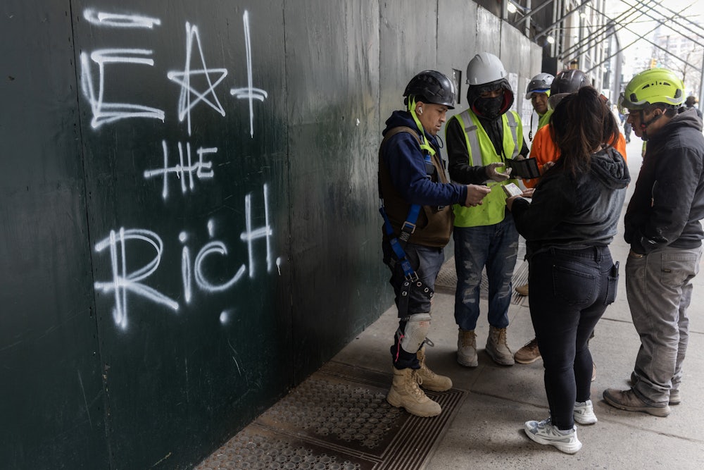 Construction workers settle their lunch bills next to graffiti scrawled on the wall of a construction site reading "eat the rich"  in New York City.